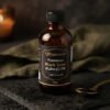 An amber glass bottle of cold pressed black seed kalonji oil with rich dark seeds around it in low warm lighting.