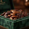 Crinkled premium organic Mamra almonds displayed on a rich green velvet luxury container, with golden almond oil glistening on surface, warm dark background