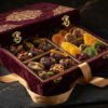 Extravagant royal velvet gift box opened with compartments filled with stuffed dates and exotic dried fruit treats tied with golden silk ribbon.