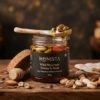 Honista jar presented open on a hand-carved walnut tabletop with a ceramic spoon coated in wild mountain honey and scattered premium raw pistachios and Mamra almonds against a warm roasted charcoal and gold ambient backdrop.