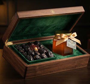 Luxurious dark walnut box lined with royal green velvet containing Madinah Ajwa dates and a hexagonal jar of raw golden Sidr honey tied with golden ribbon, warm golden lighting studio food photography