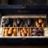 Seven varieties of holy Islamic dates arranged symmetrically in a velvet presentation box including Ajwa Al-Madinah, Kalmi, and Mabroom