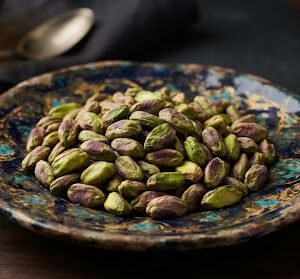 Shelled green Iranian Pistachio kernels piled on handcrafted antique plate, soft diffused luxury lighting